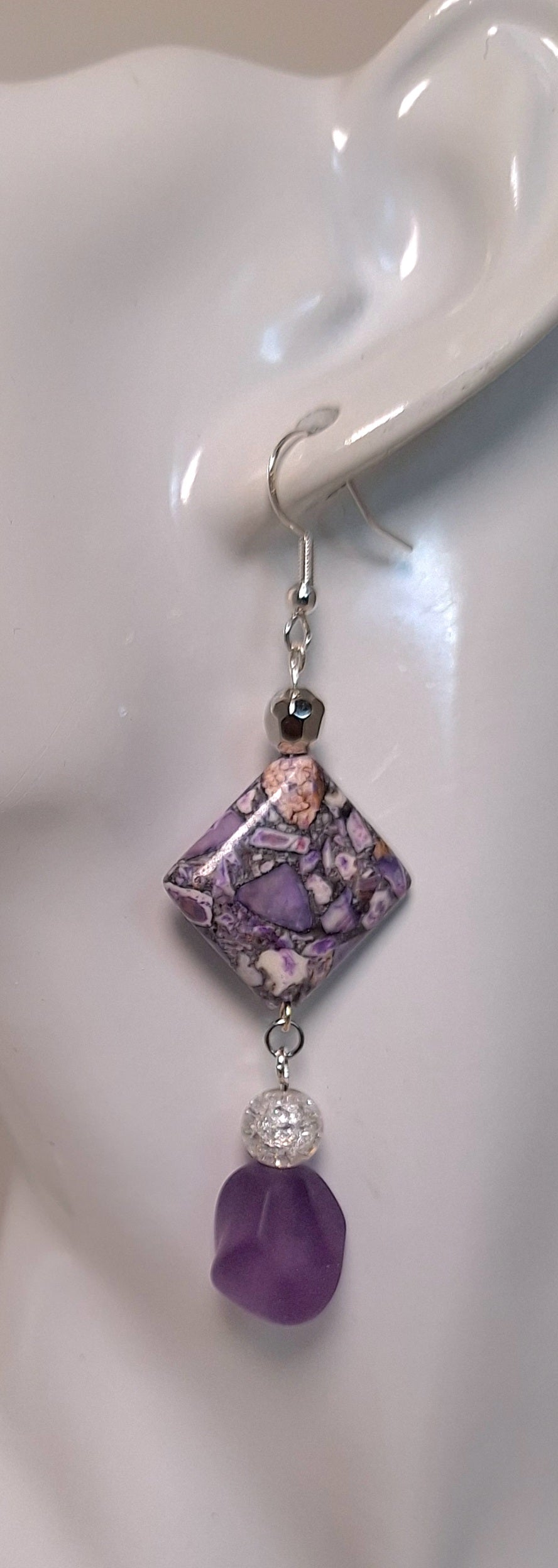 Close-up view - The design includes 1 diamond shaped soft purple printed earring with a marbleized look, 1 coordinating frosted bead in a matt finish, 1 cracked glass and 1 silver bead.
Measuring approx. 2" not including the Sterling silver ear wires. 