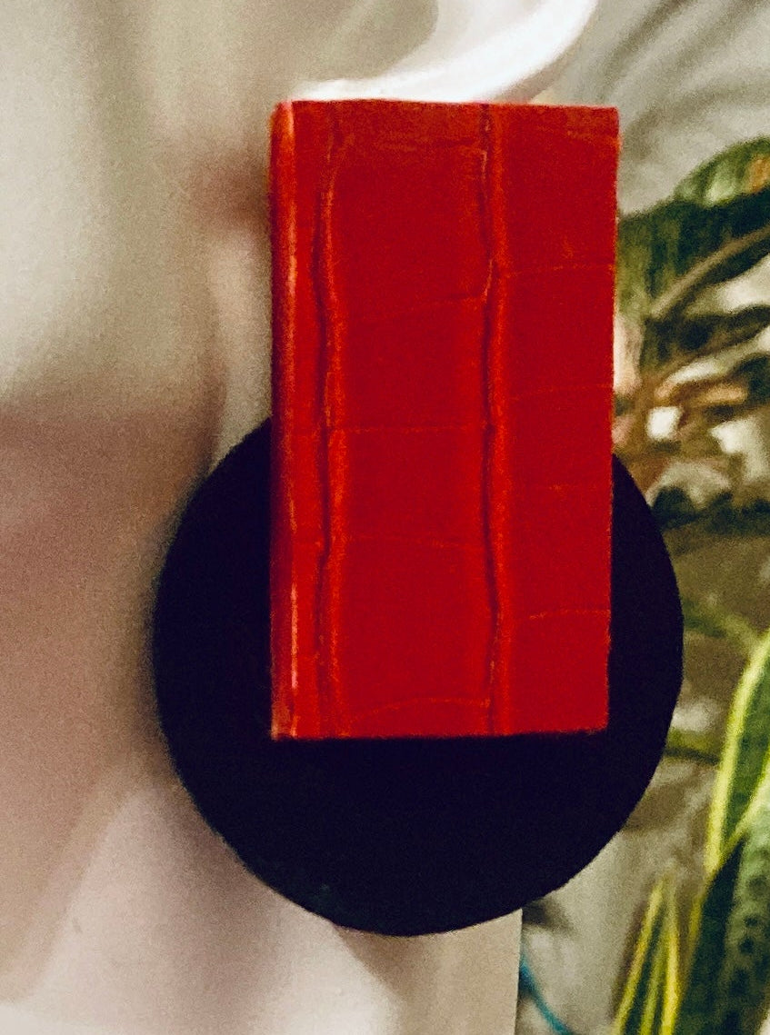 A pair of geometric drop earrings displayed on a white mannequin head. The earrings feature a large, textured red rectangular top section mounted on a round black base, set against a white background.