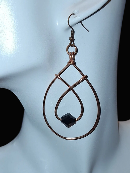 Double copper wire earring in a tear drop shape paired in smaller hoop with a black glass bead. Finished with copper ear wires, on a white mannequin.