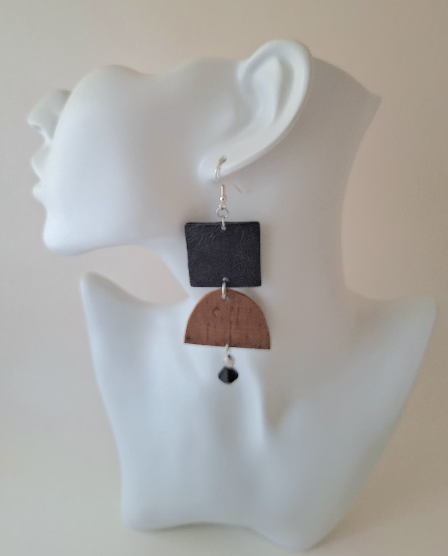 A textured black square paired with a curved brown cork accent, silver bead, and black glass drop on a white mannequin head. Crafted with hypoallergenic ear wires for comfort and designed to be an affordable everyday staple at $15.00.