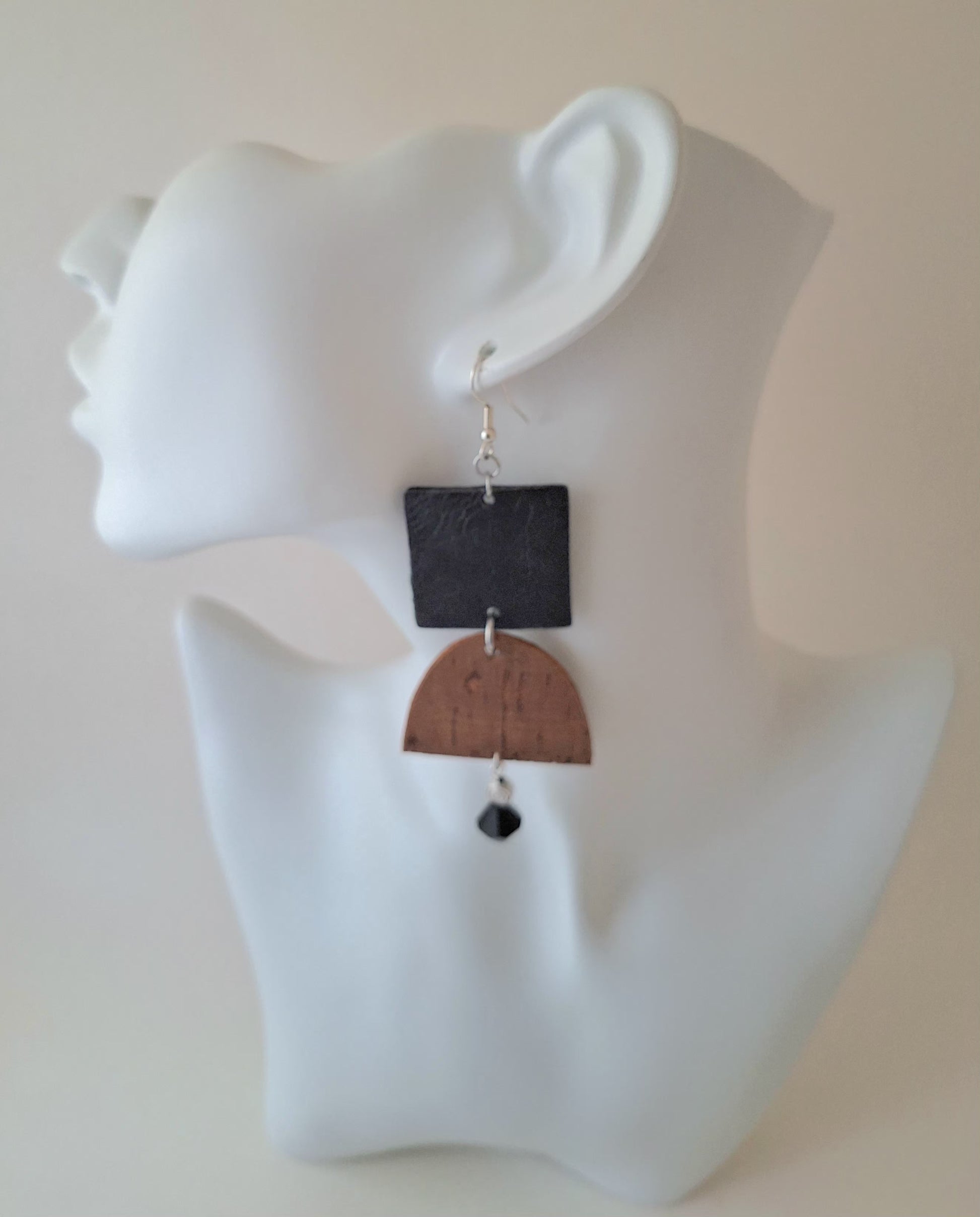  A textured black square paired with a curved brown cork accent, silver bead, and black glass drop on a white mannequin head. Crafted with hypoallergenic ear wires for comfort and designed to be an affordable everyday staple at $15.00.