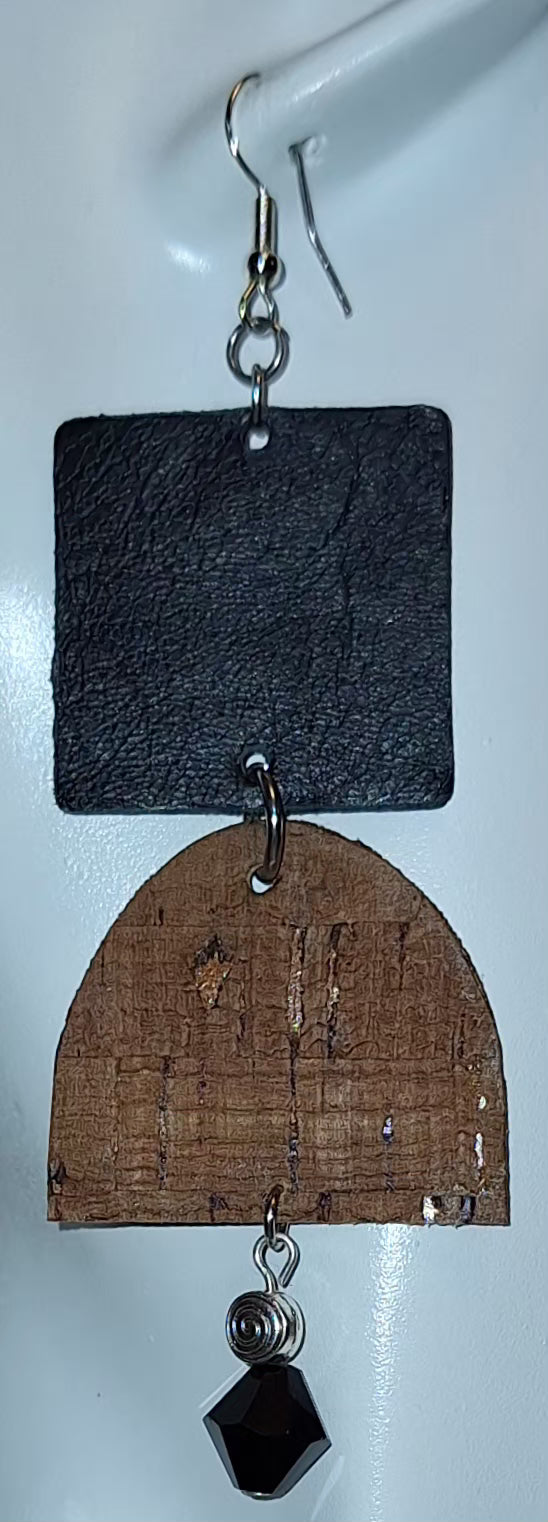  A textured black square paired with a curved brown cork accent, silver bead, and black glass drop on a white mannequin head. Crafted with hypoallergenic ear wires for comfort and designed to be an affordable everyday staple at $15.00.