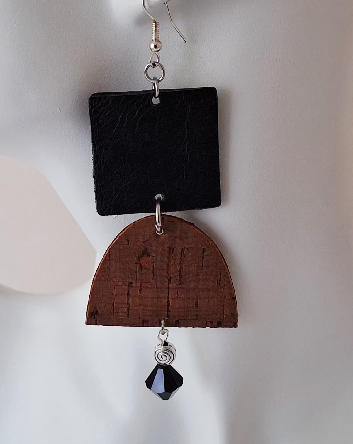  A textured black square paired with a curved brown cork accent, silver bead, and black glass drop on a white mannequin head. Crafted with hypoallergenic ear wires for comfort and designed to be an affordable everyday staple at $15.00.