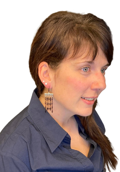 Woman wearing a blue shirt wearing Silver bar-type earrings with black dangles in various shapes on a white background