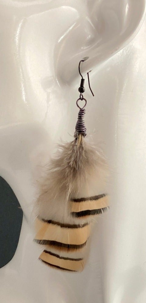 Feather earrings on a white mannequin head. Colors include Smoke, Gold and Black. Paired with bronze hypoallergenic wires. Very lightweight. 